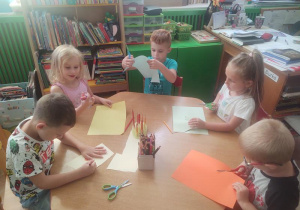 Dzieci przy czerwonym stoliku odrysowują swoje dłonie