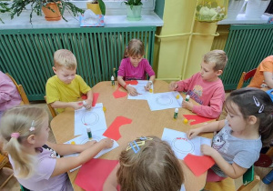 Dzieci przy zielonym stoliku wyklejają czerwoną wydzieranką wzory litery "o"