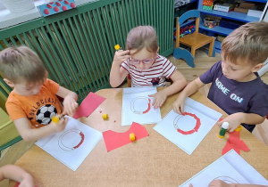 Dzieci przy czerwonym stoliku wyklejają czerwoną wydzieranką wzory litery "o"