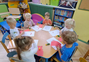 Dzieci przy niebieskim stoliku wyklejają czerwoną wydzieranką wzory litery "o"