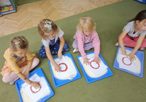 Klara, Gabryś, Gabrysia i Hania "rysują" literę "o" palcami po wyklejonych wzorach, śpiewając piosenkę "Ola"