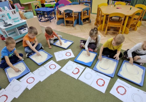 Przedszkolaki "rysują" literę "o" palcami na kaszy mannie, śpiewając piosenkę "Ola"