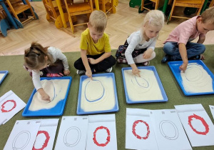 Marysia, Filip, Hania, Jaś i Misia "rysują" literę "o" palcami na kaszy mannie, śpiewając piosenkę "Ola"