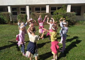 Dzieci w kole tańczą z podniesionymi rękami w górze