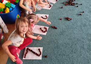 Dzieci siedzą na dywanie, układają cyfry z kasztanów