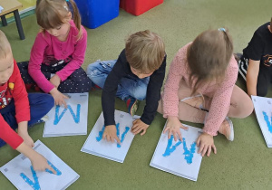 Dzieci za pomocą dotyku doświadczają faktury wyklejonych wzorów litery "M"