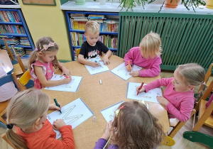 Dzieci przy żółtym stoliku kreślą litery "M" mazakami, jednocześnie śpiewając piosenkę "Małgorzata"