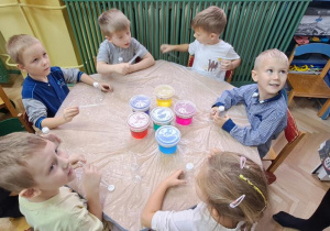 Dzieci przy czerwonym stoliku przygotowują się do eksperymentów z kolorową wodą