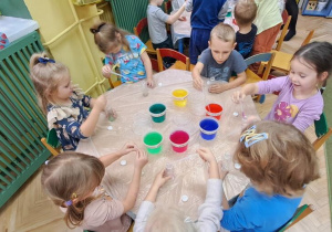 Dzieci przy zielonym stoliku rozpoczynają eksperymentowanie z kolorową wodą