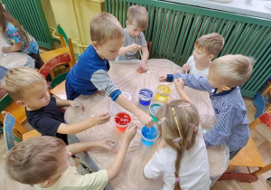 Dzieci przy czerwonym stoliku rozpoczynają eksperymentowanie z kolorową wodą