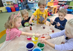 Dzieci przy żółtym stoliku kończą tworzyć kolorowe eliksiry