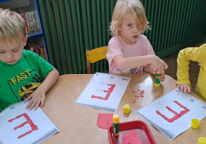 Gabrysia, Tymek i Lena wyklejają litery "E" czerwoną wydzieranką