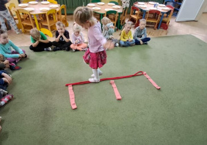 Klara spaceruje po literze "E" ułożonej z liny i szarf