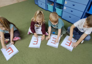 Marysia, Oliwka, Antek i Filip paluszkami "rysują" literę "E" na wzorach, śpiewając piosenkę "Ewelina"