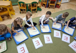 Dzieci kreślą palcami litery "E" na mannie, jednocześnie śpiewając piosenkę "Ewelina"