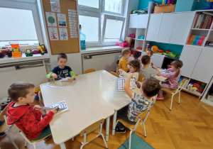 Dzieci siedzą przy stolikach, wycinają nożyczkami sylwetę plecaka