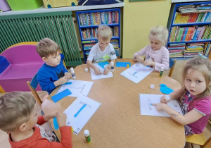 Dzieci przy niebieskim stoliku wyklejają niebieską wydzieranką wzory litery T
