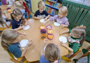 Dzieci przy żółtym stoliku robią owocowe szaszłyki