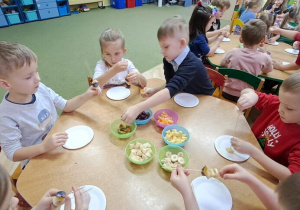 Dzieci przy czerwonym stoliku robią owocowe szaszłyki