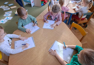 Dzieci przy żółtym stoliku kreślą litery "K" na kartkach w rytmie piosenki "Krystyna"