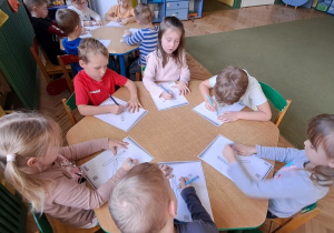 Dzieci przy zielonym stoliku kreślą litery "K" na kartkach w rytmie piosenki "Krystyna"