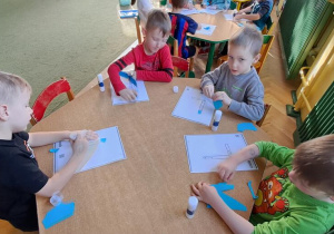 Dzieci przy czerwonym stole wyklejają litery "L" niebieską wydzieranką