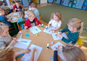 Dzieci przy żółtym stole wyklejają litery "L" niebieską wydzieranką