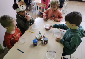 Dzieci siedzą przy stolikach z przygotowanymi elementami do tworzenia slime