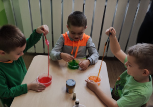 Dzieci siedzą przy stolikach, przygotowują masę na slime