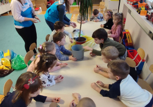 Dzieci przy stolikach przesadzają kwiat