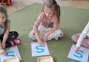 Marysia, Klara i Laura "rysują" palcami literę "S" na wzorach do piosenki "Sławek"