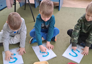 Stasio, Mateusz i Antoś "rysują" palcami literę "S" na wzorach do piosenki "Sławek"
