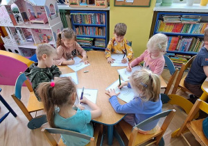 Dzieci przy niebieskim stoliku rysują literę "S" na kartkach podczas piosenki "Sławek"