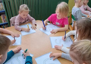 Dzieci przy żółtym stoliku rysują literę "S" na kartkach podczas piosenki "Sławek"