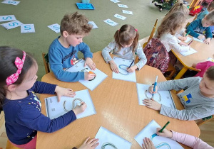 Dzieci przy zielonym stoliku rysują literę "S" na kartkach podczas piosenki "Sławek"