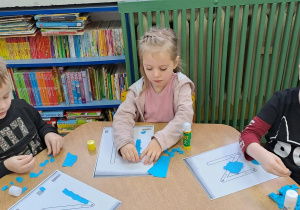 Tymek, Mateusz i Lena wyklejają wzory liter "N" niebieską wydzieranką