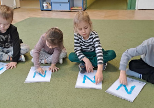 Tymek, Remik, Daniela i Oskar odtwarzają litery "N" na wyklejonych wzorach w rytmie piosenki "Natalia"