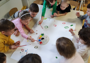 Dzieci na arkuszu papieru malują farbami kropki, koła