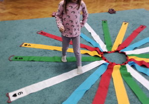 Lucynka utrwala rytmy z wykorzystaniem kolorowego wiatraka matematycznego rozłożonego na dywanie