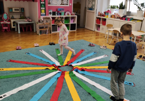 Wojtek i Julka utrwalają rytmy z wykorzystaniem kolorowego wiatraka matematycznego rozłożonego na dywanie