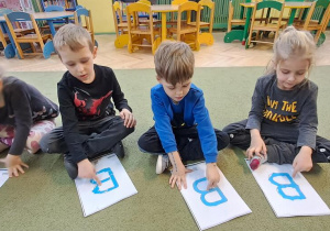 Marysia, Janek, Filip, Remik kreślą palcami na wyklejonych wzorach litery "B" w rytmie piosenki "Bronisław"