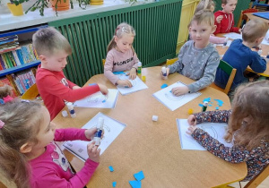 Dzieci przy żółtym stole wyklejają wzory litery "G" niebieską wydzieranką