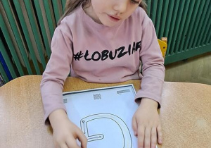 Lena pisze literę "G" na kartce w rytmie piosenki "Grzegorz"