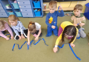 Dzieci układają litery "W" z niebieskich wstążek