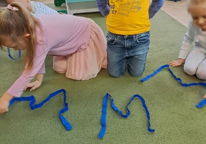 Klara i Mateusz układają ze wstążek litery "W"