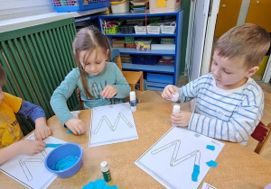 Mateusz, Oliwka i Antek wyklejają niebieską wydzieranką wzory litery "W"