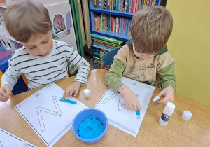 Olaf i Filip wyklejają niebieską wydzieranką wzory litery "W"