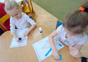 Nadia i Marysia wyklejają niebieską wydzieranką wzory litery "W"