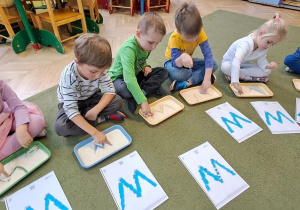 Dzieci rysują litery "W" na tackach z kaszą w rytmie piosenki "Weronika"