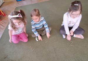 Marysia, Remik i Oliwka układają z zapałek litery "Z"